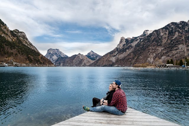 Man and woman sitting by a lake and mountains