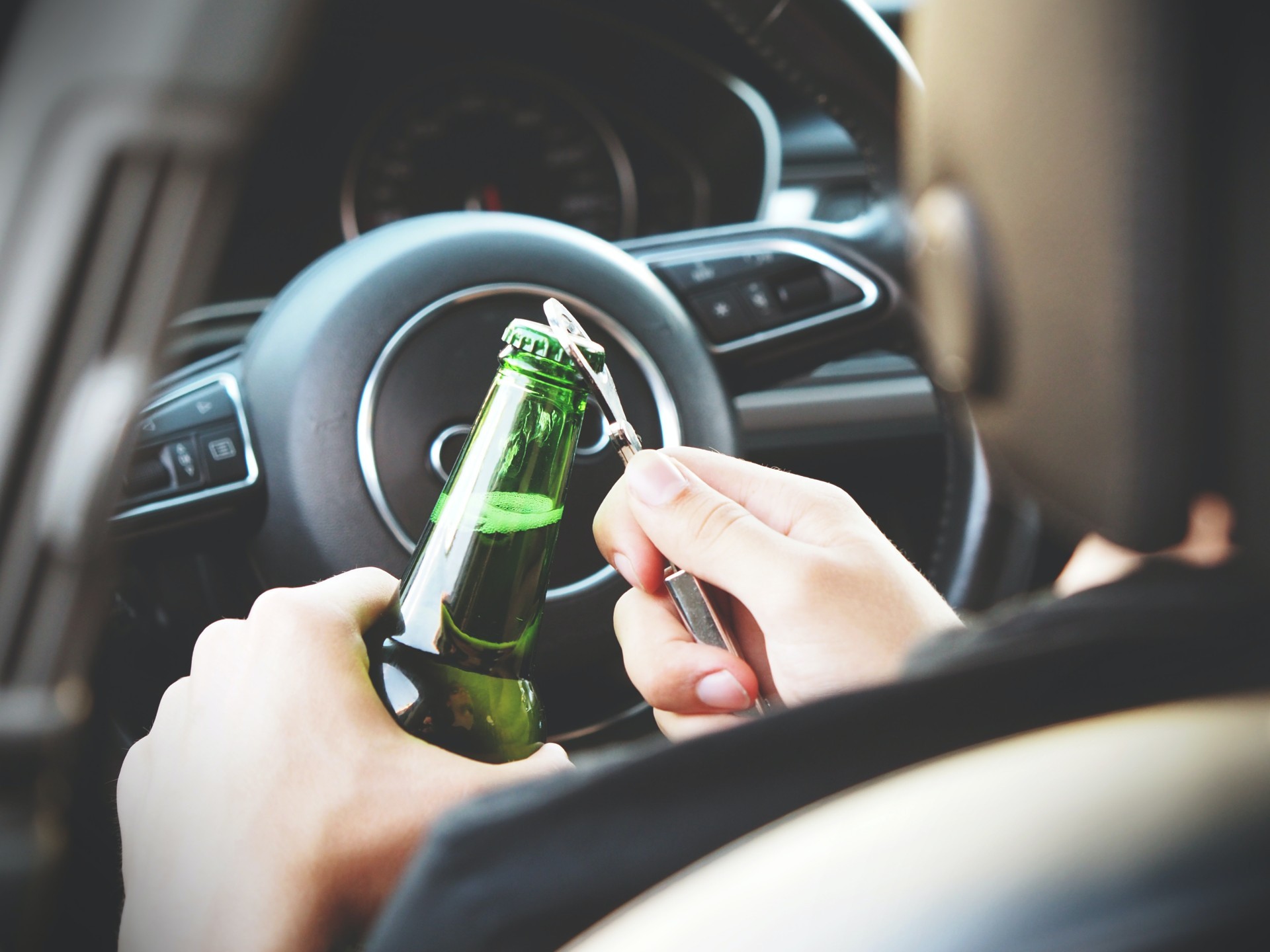 Driver opening bottle of beer behind the wheel