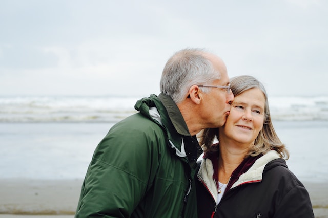 husband kissing wife on the cheek, on a beach