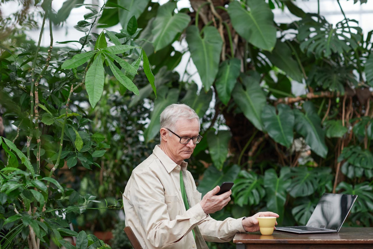 Older man sitting by plants, holding his mobile phone