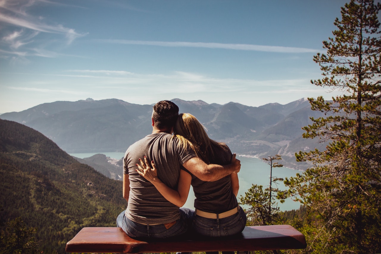 Man and woman embracing on bench outside, looking at mountains