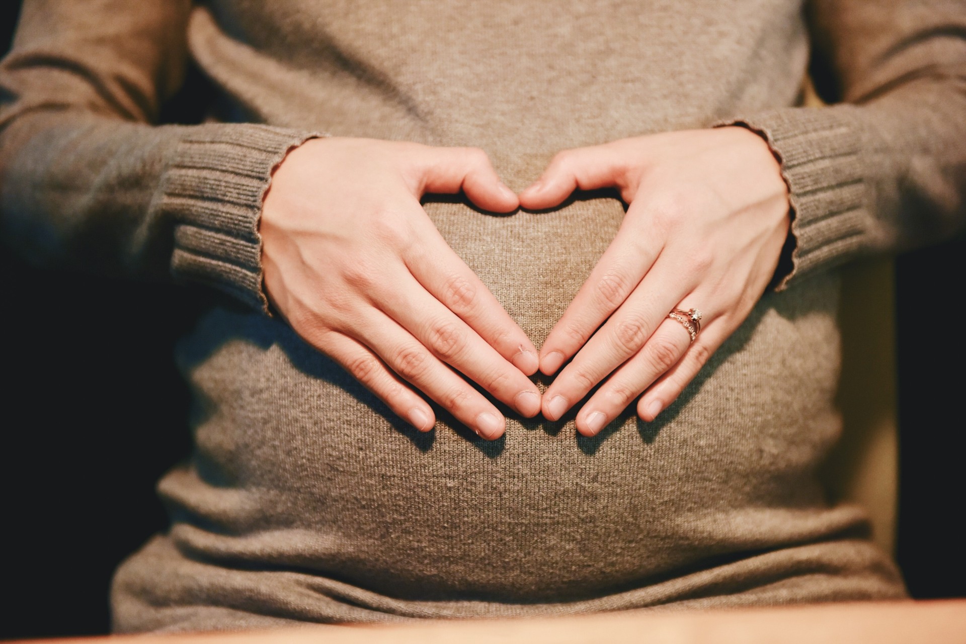 A hand forming a heart over a pregnant belly